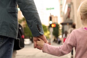 Une petite fille dinne la main à son père dans la rue